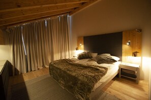 Quarto com teto de madeira, cama com manta de pele, mesa de cabeceira com abajur e janela com cortinas.
