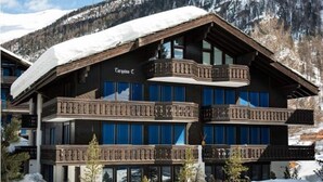 A multi-story hotel with balconies and large windows, surrounded by snow and mountains.