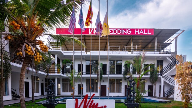 A wedding hall with a modern architectural design, featuring a prominent entrance and multiple flags. - WM Hotel Arugambay (Arugam Bay)