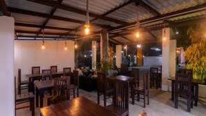 A restaurant with wooden tables and chairs, hanging light fixtures, and potted plants. - WM Hotel Arugambay (Arugam Bay)