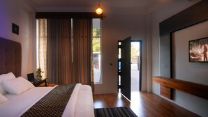 A modern hotel room with a large bed, a desk with a laptop, a painting on the wall, and a view through an open door. - WM Hotel Arugambay (Arugam Bay)