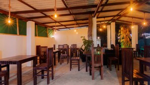A restaurant with wooden tables and chairs, hanging lights, and a large plant. - WM Hotel Arugambay (Arugam Bay)