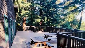 A wooden deck with picnic tables and a wooden fence, surrounded by trees. - Wildwood a great family house Sleeps up to 10!  Walk to trails! (Inverness)