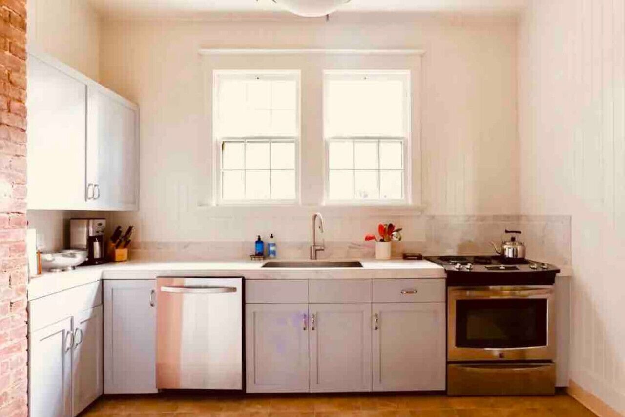 A compact kitchen with white cabinets, a dishwasher, a double sink, and a stove.