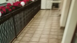 A corridor with tiled flooring, a metal railing, and a white wall.