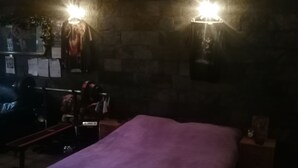 A dimly lit room with a bed, a bench, and a wall-mounted shelf.