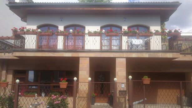 A two-story building with a balcony, potted plants, and a gated entrance.