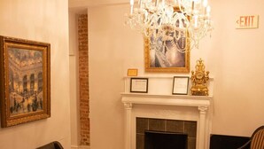 A room with a fireplace, a chandelier, a framed picture, and two chairs.
