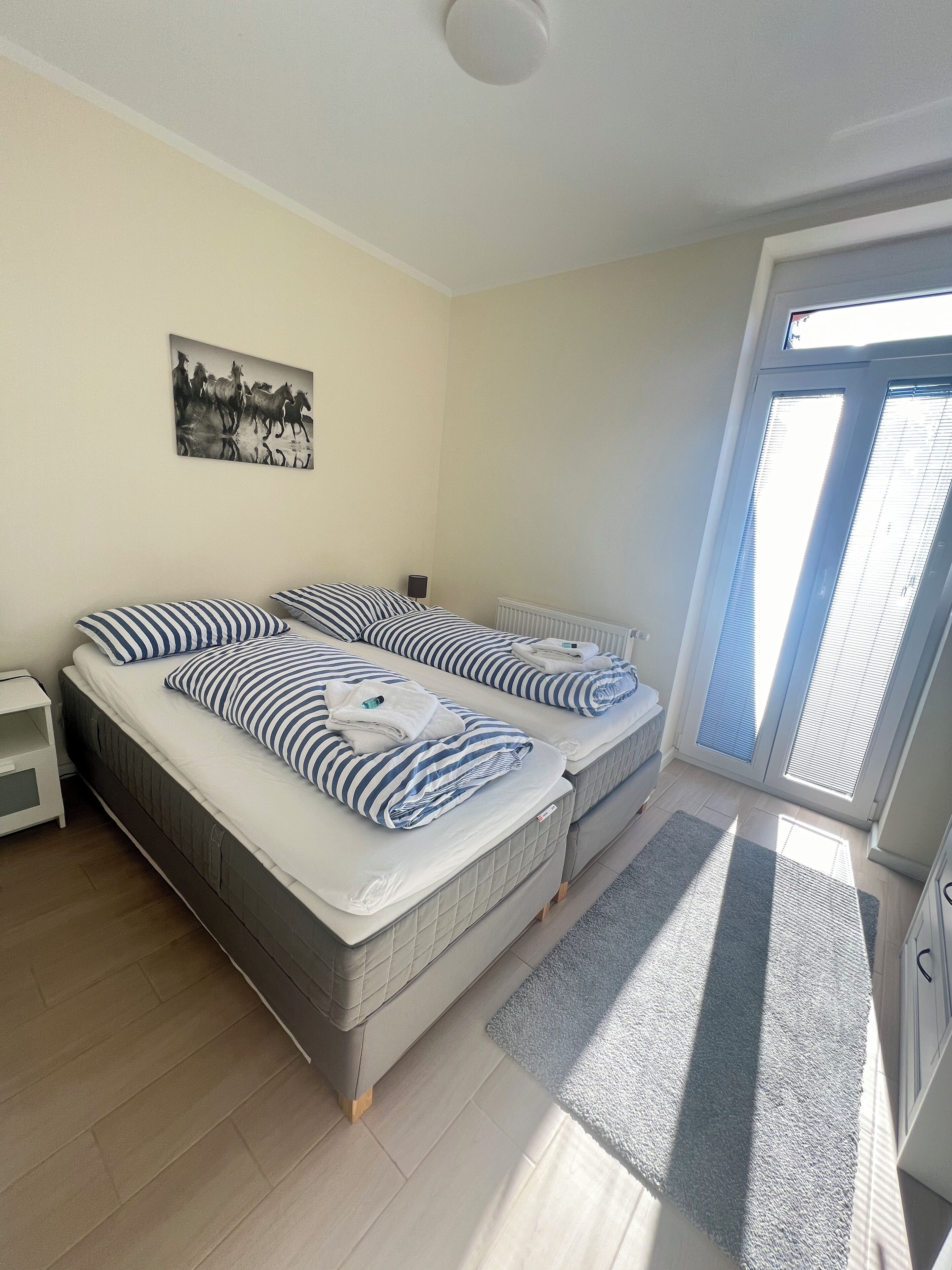 Una habitación con dos camas, un radiador, un cuadro en la pared y una ventana con persianas.