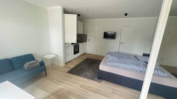 A compact living space with a kitchenette, a sofa, a bed, and a small table.