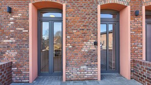 Un bâtiment en briques doté de deux grandes portes vitrées et d’un petit porche.