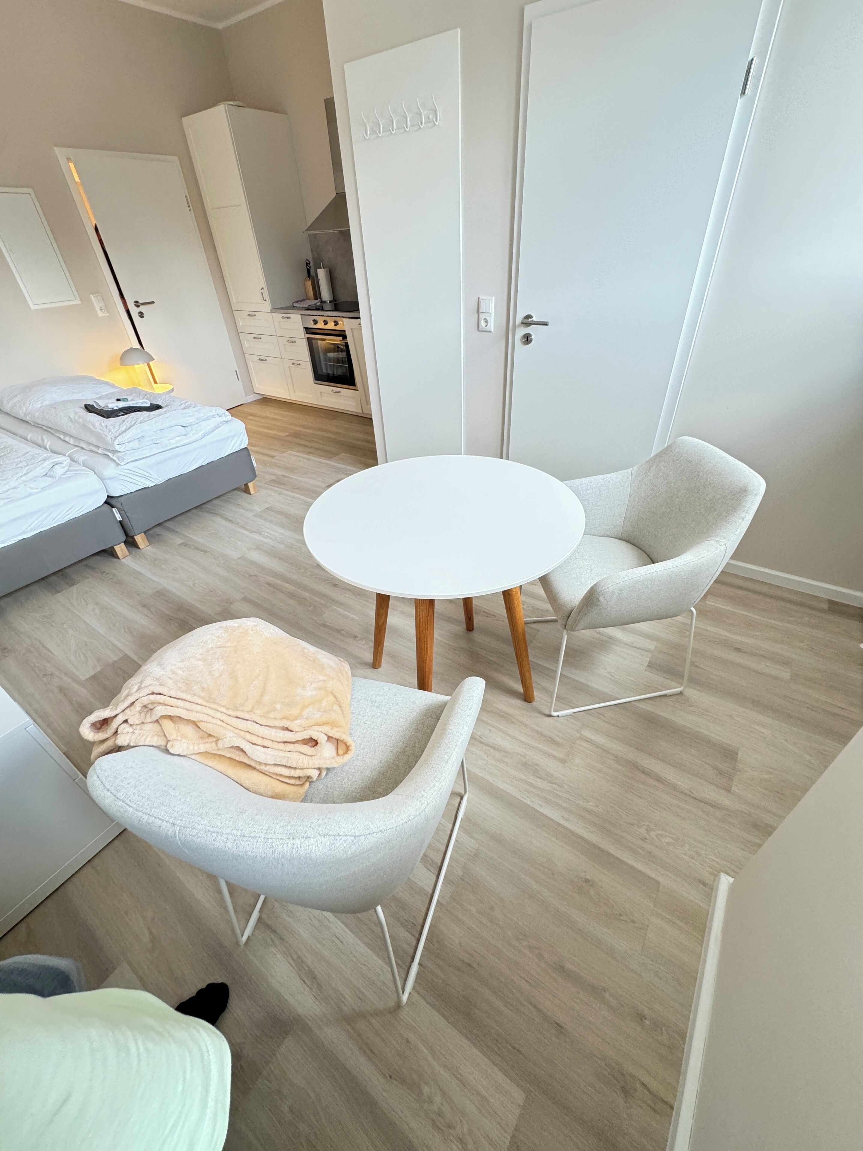 Une chambre moderne et minimaliste, avec un lit, deux fauteuils, une table ronde et, au fond, un coin cuisine.