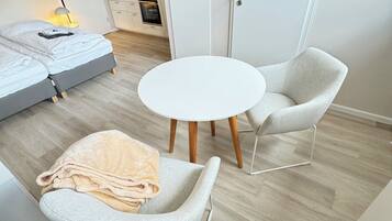 Une chambre moderne et minimaliste, avec un lit, deux fauteuils, une table ronde et, au fond, un coin cuisine.