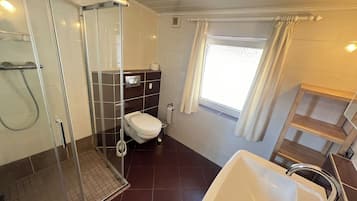 Een badkamer met een douchecabine van glas, een wit toilet, een wastafel en een raam met gordijnen.