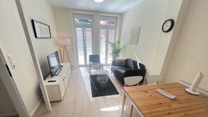 Un salon moderne avec une table à manger en bois, un canapé noir, un téléviseur et une plante.