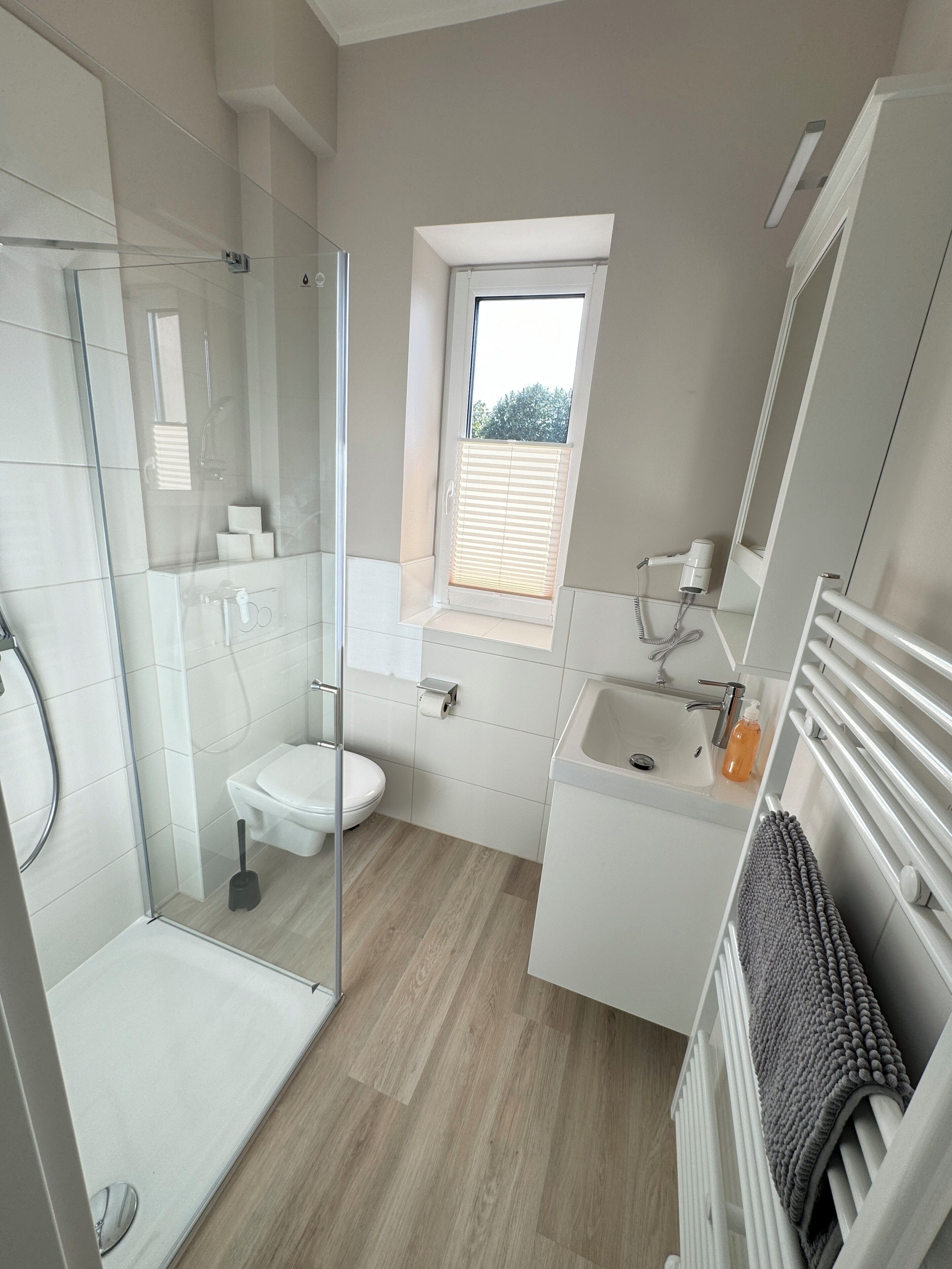 A modern bathroom with a glass shower enclosure, a toilet, a sink, and a window.