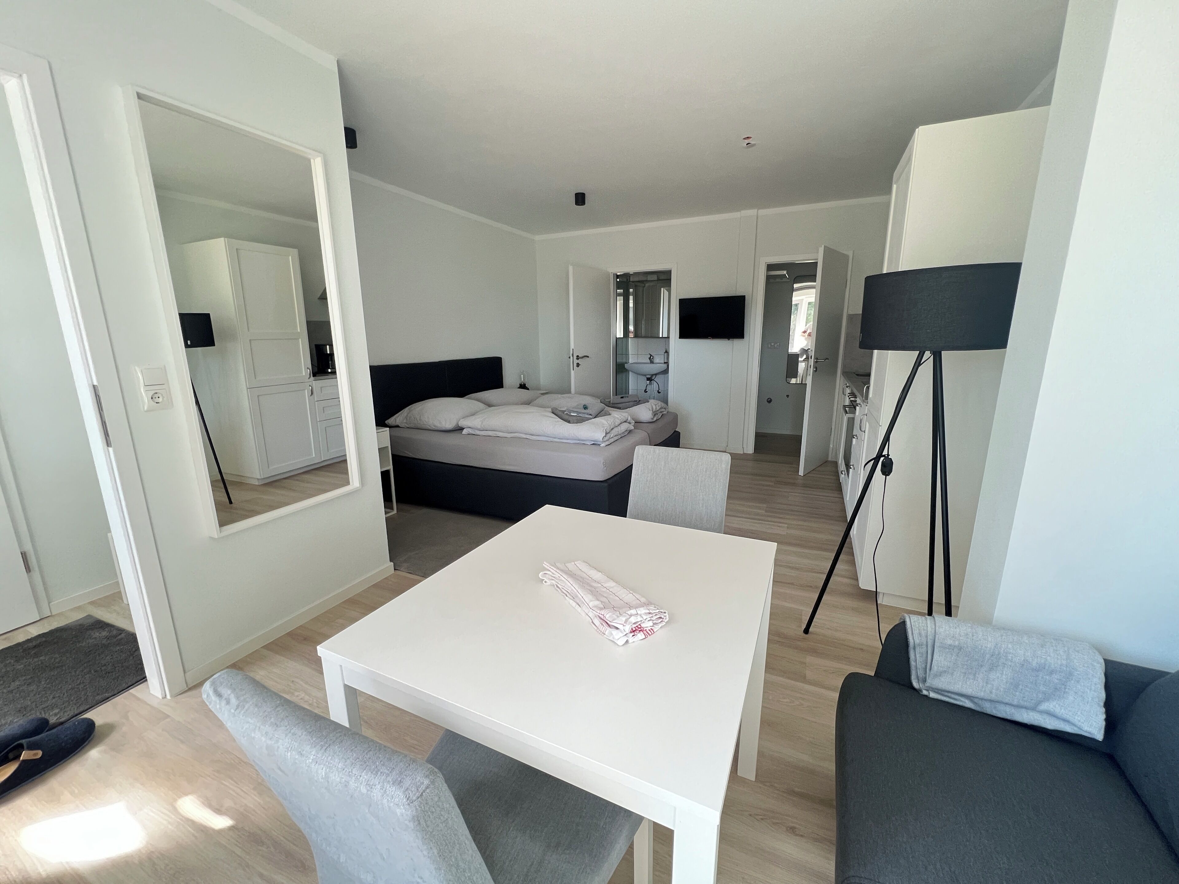 A modern hotel room with a bed, a small table, a sofa, and a mirror.