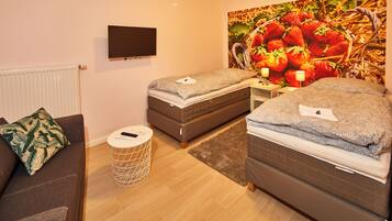 A hotel room with two beds, a TV, a large fruit-themed wall, a small round table, and a sofa.