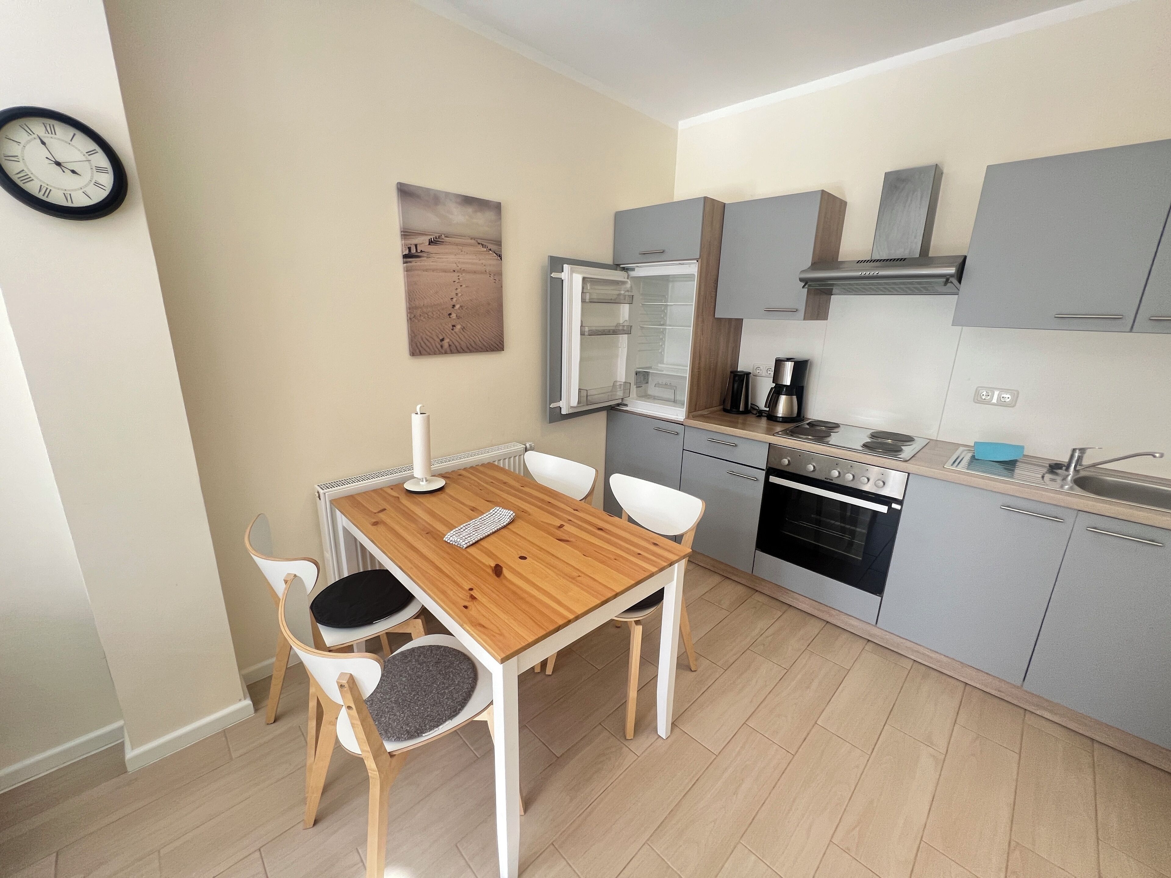 A compact kitchen with a wooden dining table, white chairs, and modern appliances.