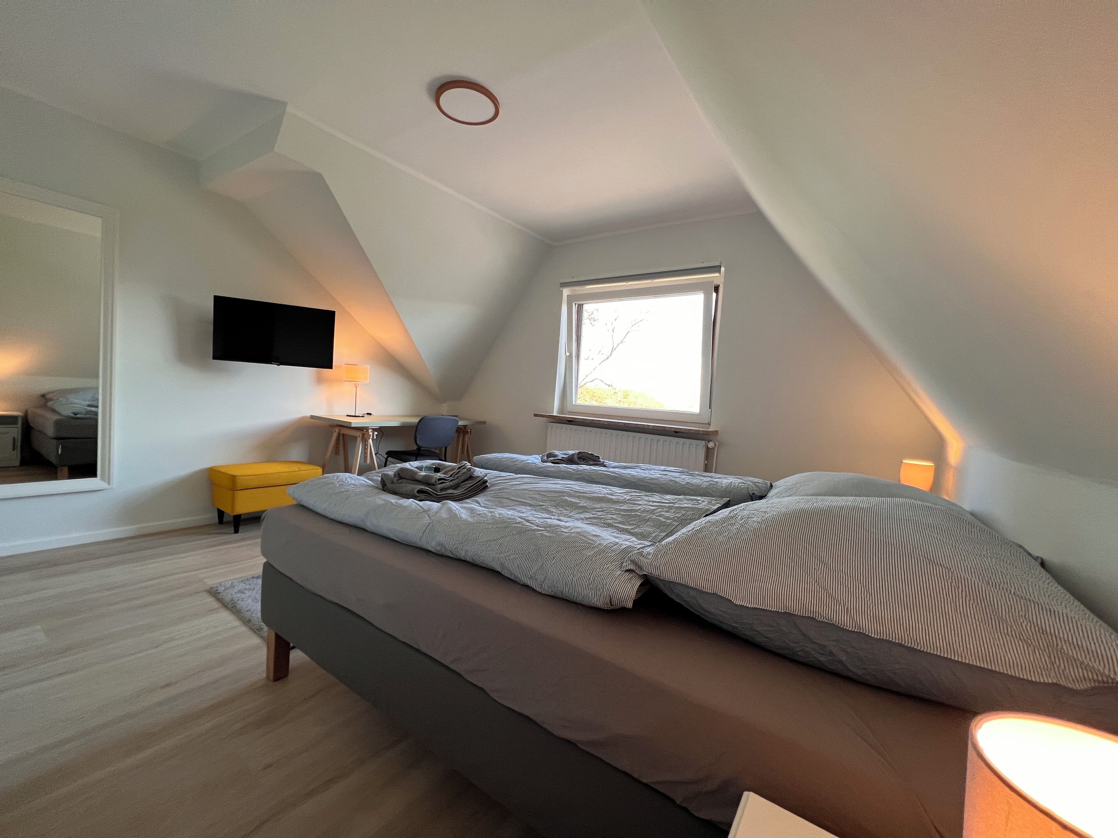 Een slaapkamer met een bed, een bureau, een stoel, een televisie, een raam en een lamp.
