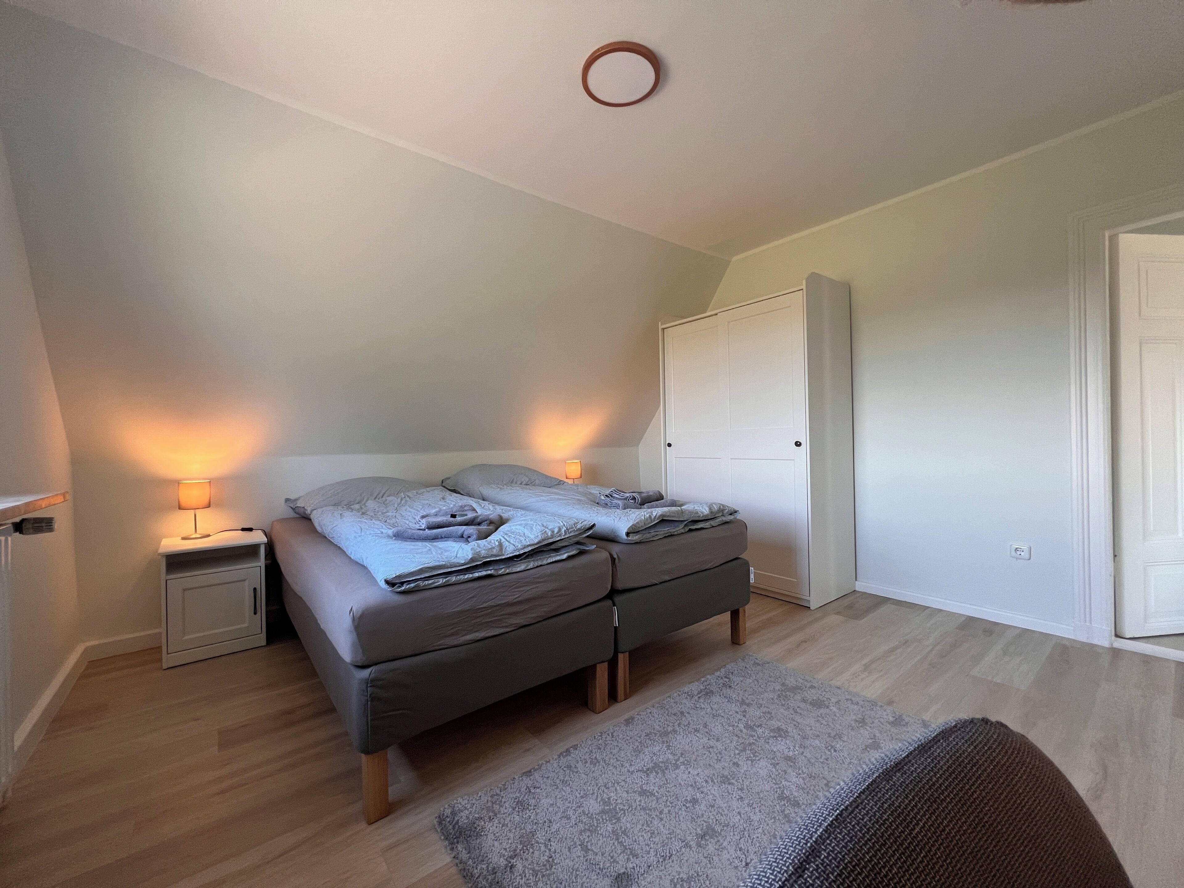 Ein Schlafzimmer mit einem Bett, Nachttischlampen, einem Kleiderschrank und einem Teppich.