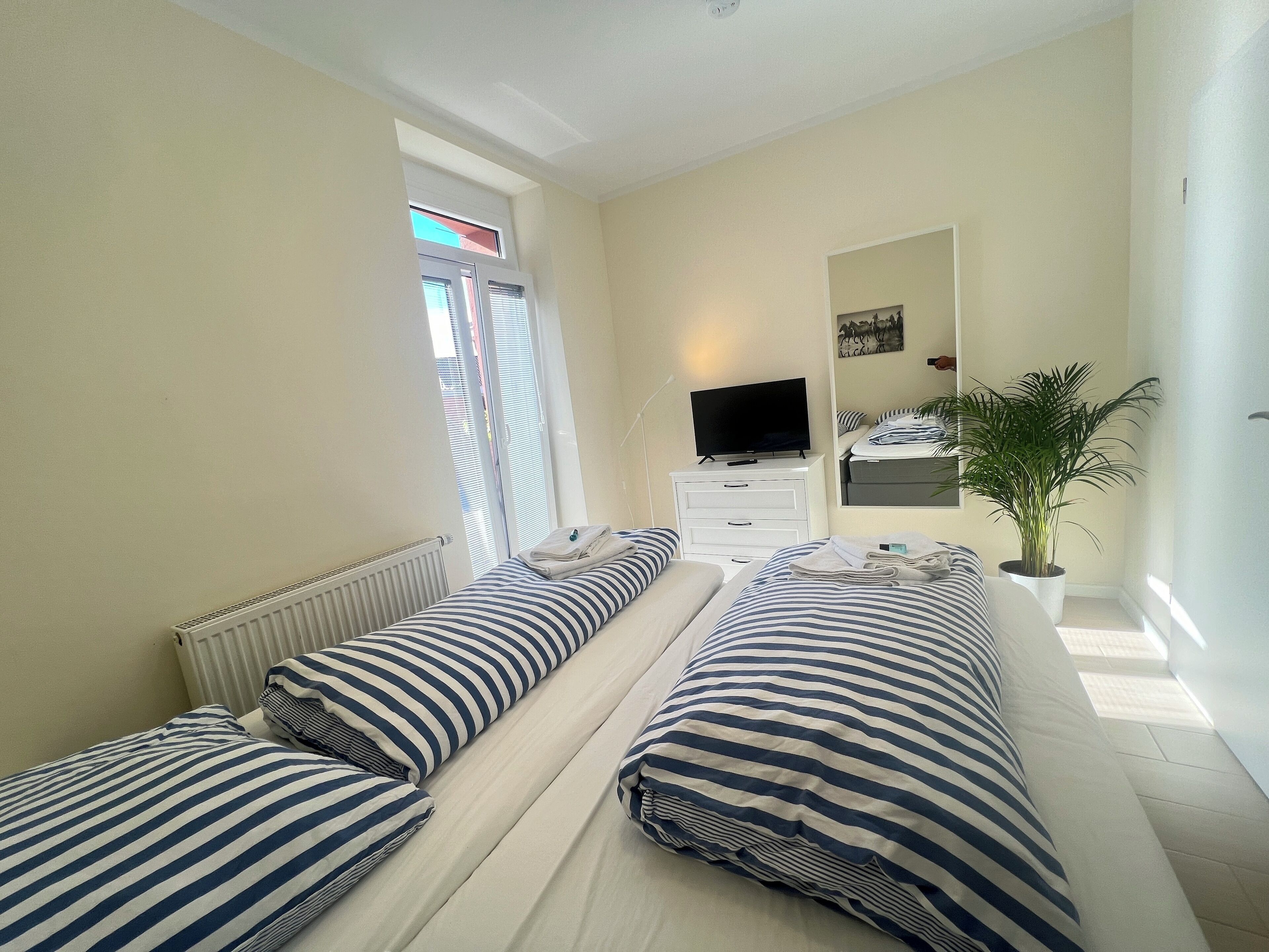 Een hotelkamer met twee bedden, een televisie, een spiegel en een potplant.