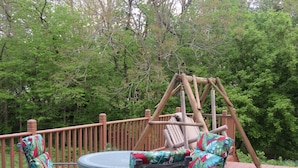 Une terrasse en bois avec une balançoire, deux chaises dotées de coussins colorés et une table.