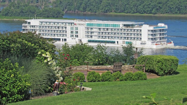 Un grand navire de croisière fluviale à plusieurs ponts, doté de balcons, est amarré à un port fluvial.