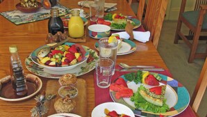 Une table à manger dressée avec différents plats, notamment des fruits, des salades et une part de tarte.