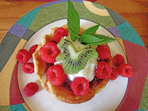 A dessert with raspberries, kiwi, and a leaf on a plate.