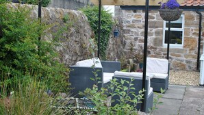 Un bâtiment en pierre doté d’un patio-jardin agrémenté de meubles en osier et d’une jardinière suspendue.