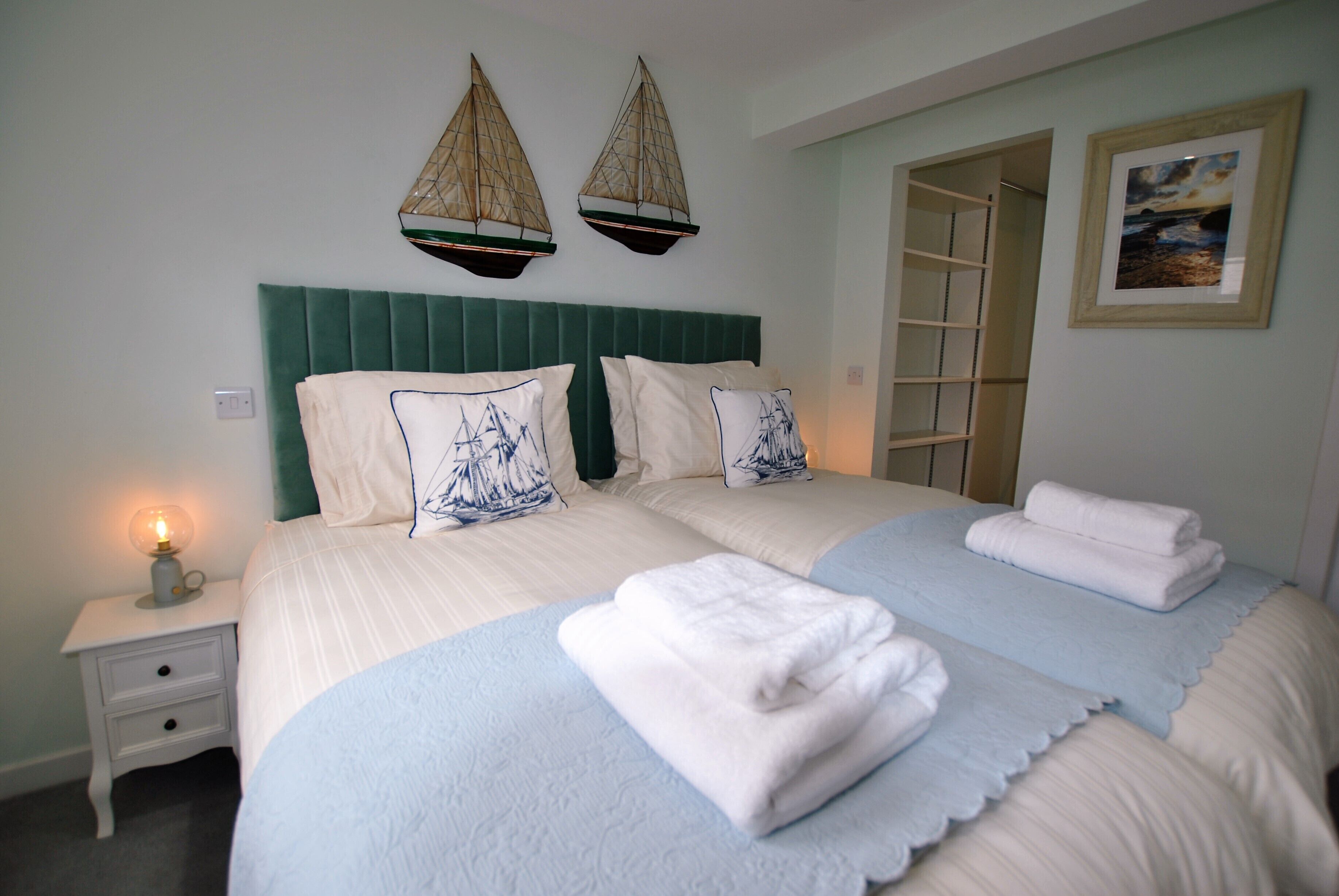A neatly made double bed with a green headboard, two decorative wall hangings, and a framed picture on the wall.