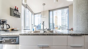 A modern kitchen with a built-in sink, a coffee maker, and a view of tall buildings. - 2BR | Gym, Pool | Bellevue | Sophari Towers M (Bellevue)