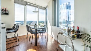 A modern kitchen with a dining area, large windows, and a view of the cityscape. - 2BR | Gym, Pool | Bellevue | Sophari Towers M (Bellevue)