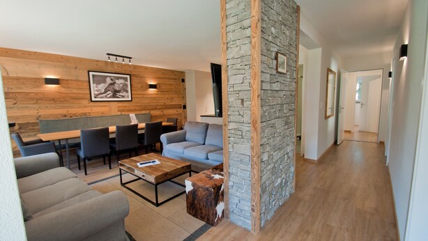 Un salon moderne avec un mur d’accent en pierre, un plafond en bois et un coin repas comprenant une table et des chaises.