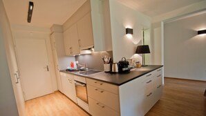 Une cuisine moderne avec des meubles blancs, un four encastré et un plan de travail sur lequel se trouvent une bouilloire et une machine à café.
