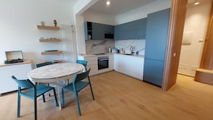 A modern kitchen with white and blue cabinets, a marble countertop, and a built-in oven. There is a dining area with a round table and blue chairs. - CaseMaggi Poets Bay Terrace with stunning views, perfect for families & friends (Portovenere)
