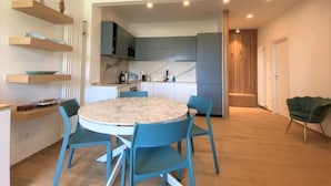 A modern kitchen with built-in appliances, a dining area with a round table and blue chairs, and a ceiling fan. - CaseMaggi Poets Bay Terrace with stunning views, perfect for families & friends (Portovenere)