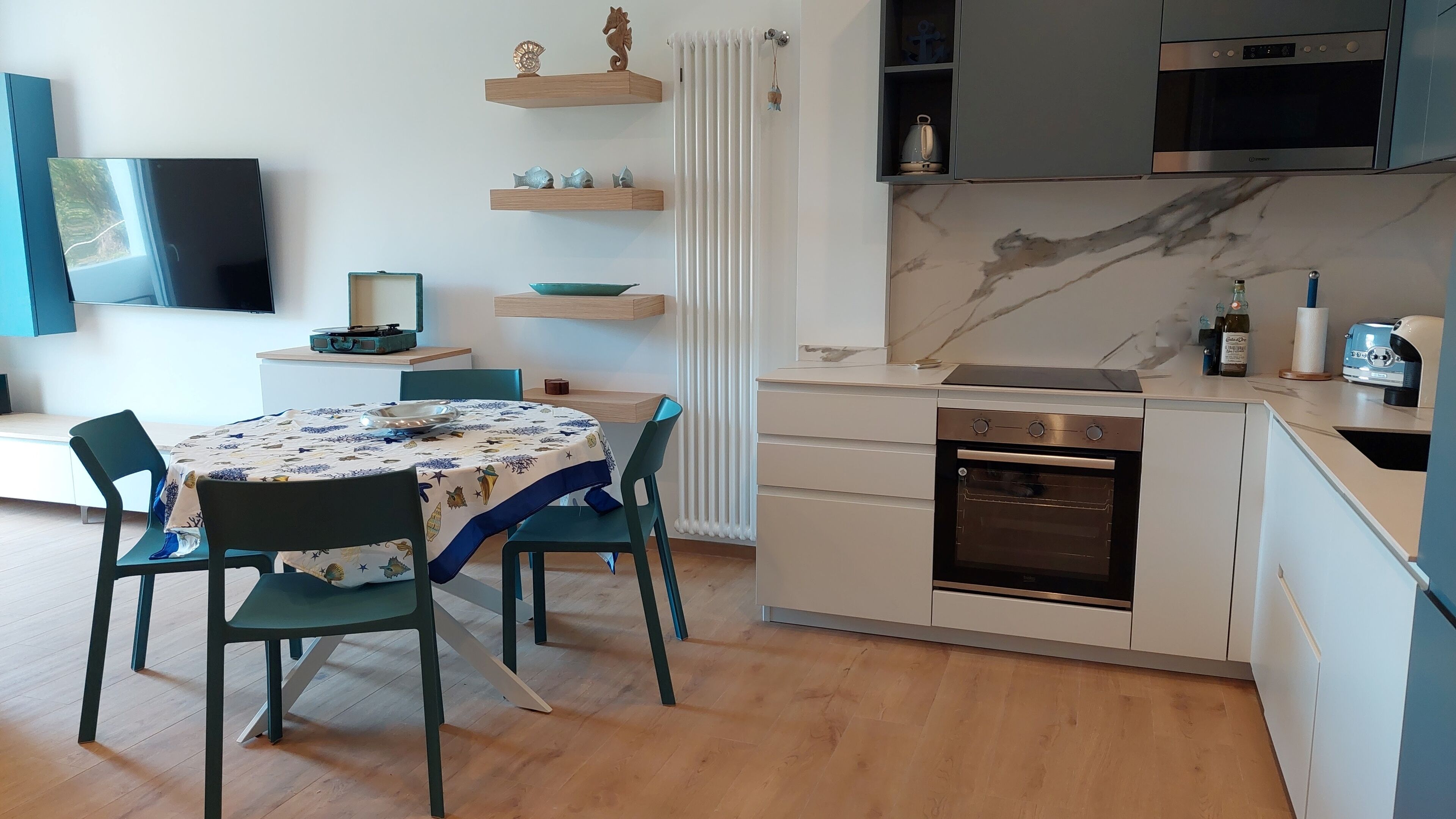 A modern kitchen with a built-in oven, a dining table with chairs, and a TV mounted on the wall.
