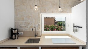 A kitchen with a stone wall, a window with a view of flowers, a coffee maker, and a knife rack. - Villa Sunset with spectacular views (Porec)