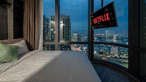 A bedroom with a large bed, a view of a cityscape through a large window, and a sign indicating the room is available for Netflix. - Landmark 81 & Vinhomes - ZEN Saigon Citypoint. (Ho Chi Minh City)
