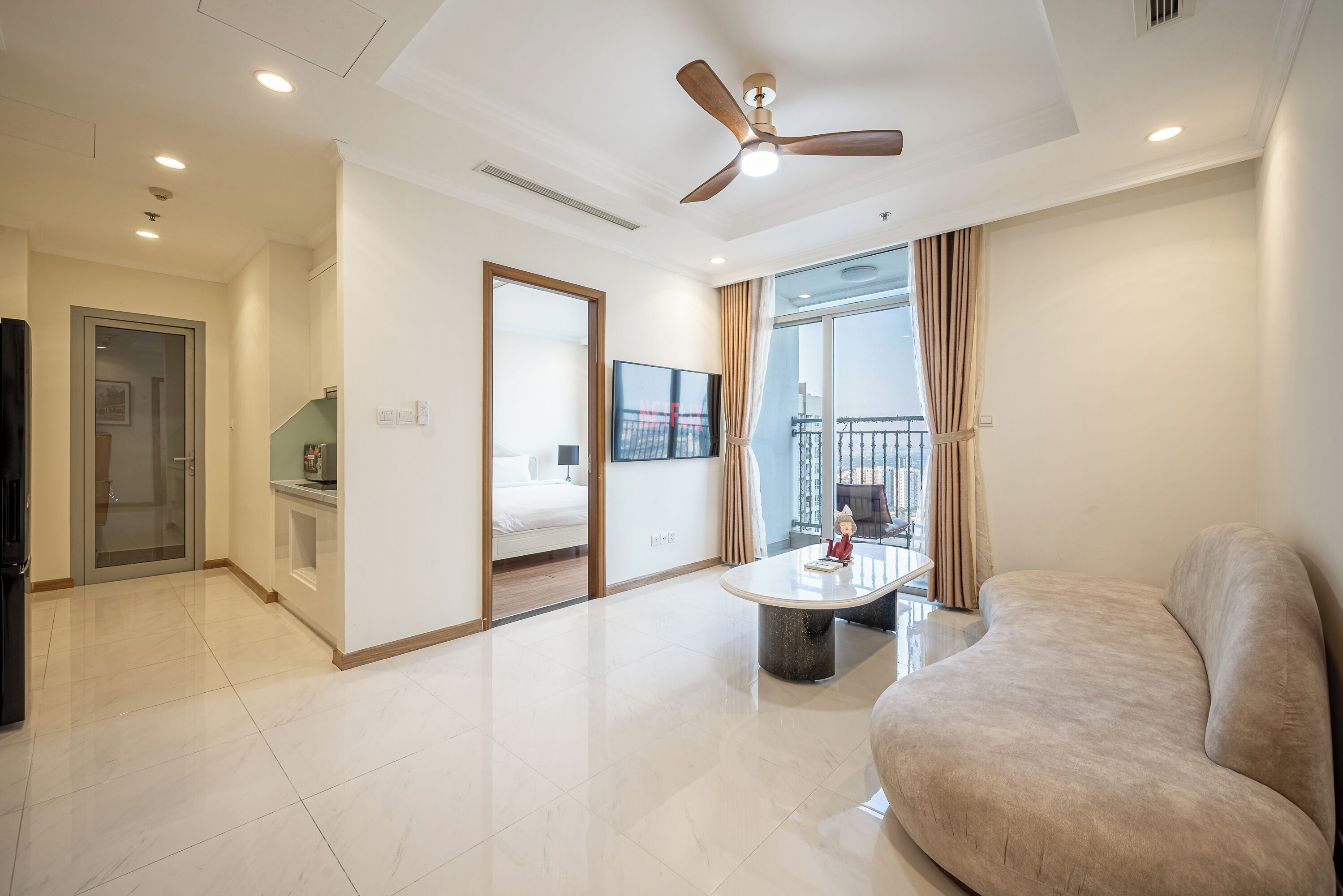 A modern hotel room with a large bed, a seating area with a table, a ceiling fan, and a balcony with a view.