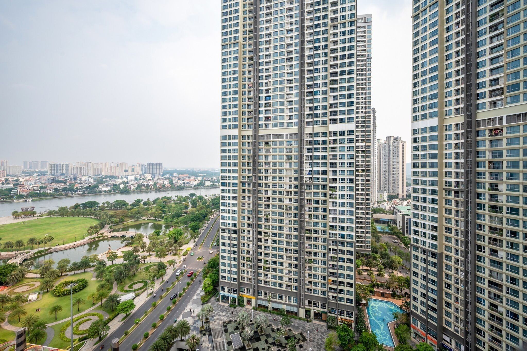 A high-rise residential building with multiple balconies, a landscaped park area with a lake, and a swimming pool.