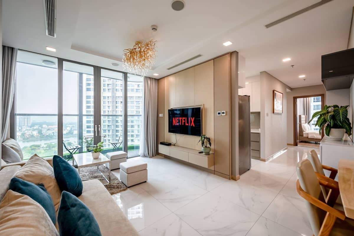 Ein modernes Wohnzimmer mit großem Fernseher, einer Couch, einem Essbereich und Blick auf eine Skyline durch große Fenster.