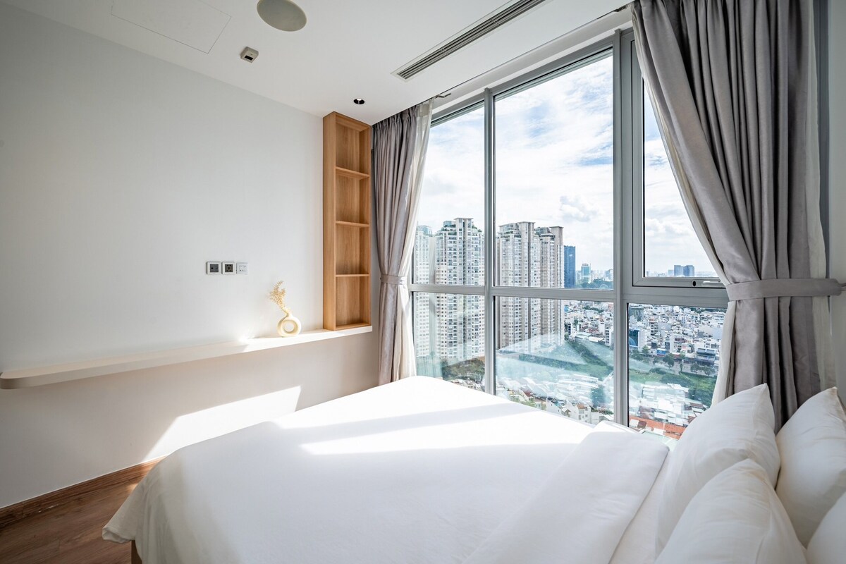 Ein modernes Hotelzimmer mit großem Fenster, einem Bett, einer Holzablage und einem kleinen Tisch.