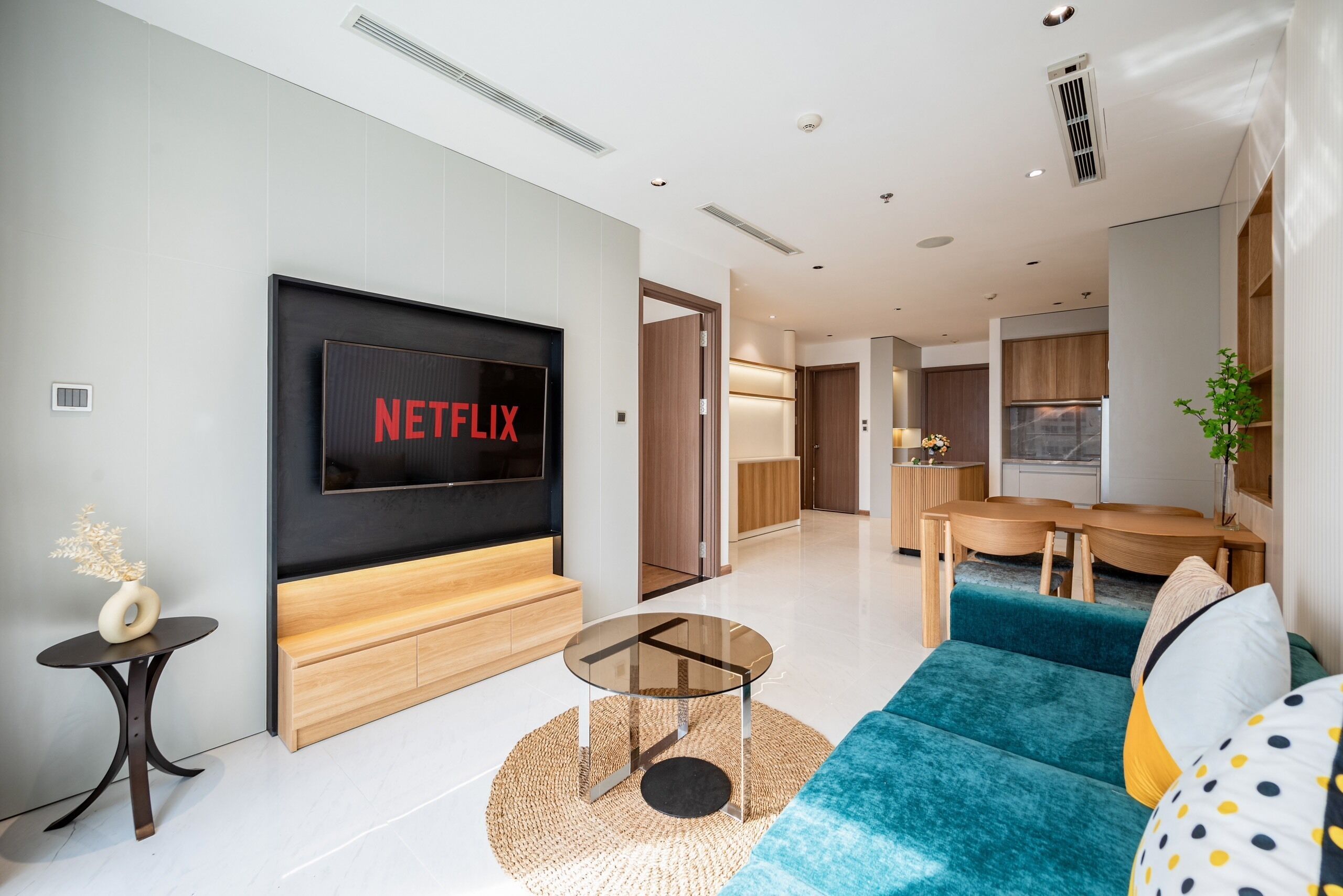 Een moderne woonkamer met een grote flatscreen-tv, een bank, een salontafel en een eethoek met houten meubels.