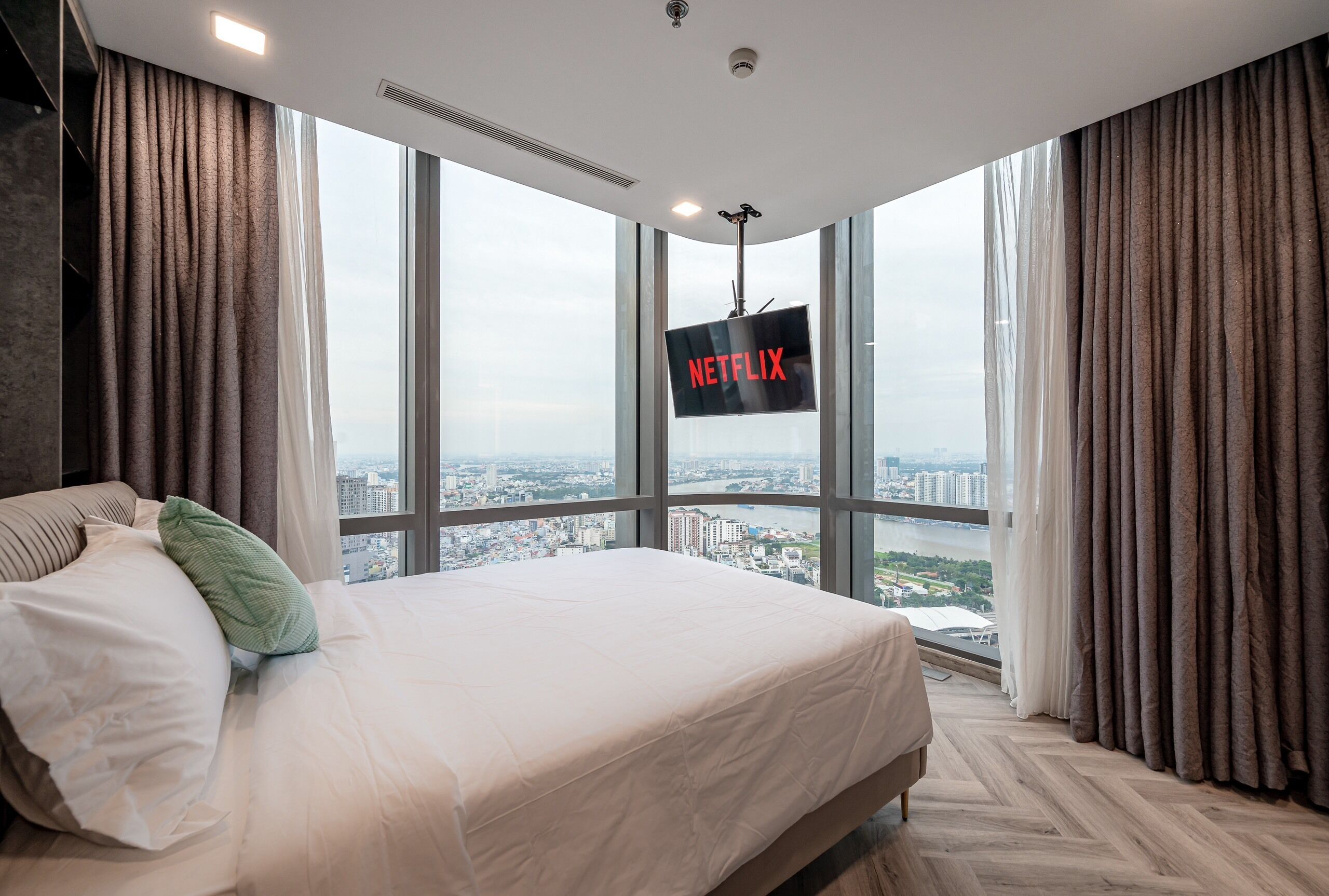 A hotel room with a large bed, a view of a cityscape, and a sign indicating a Netflix service.