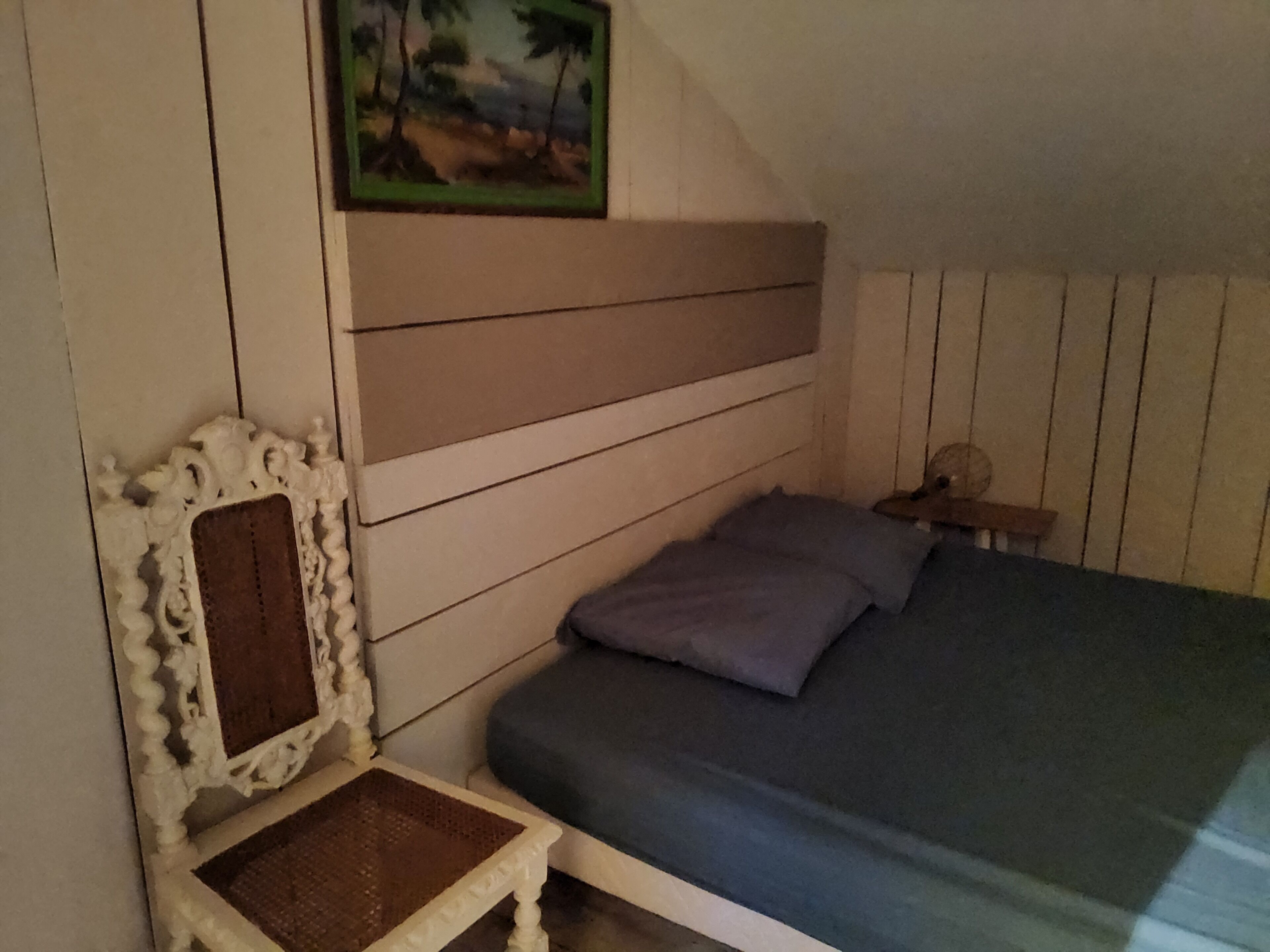 A bedroom with a bed, a chair, a nightstand, and a painting on the wall.