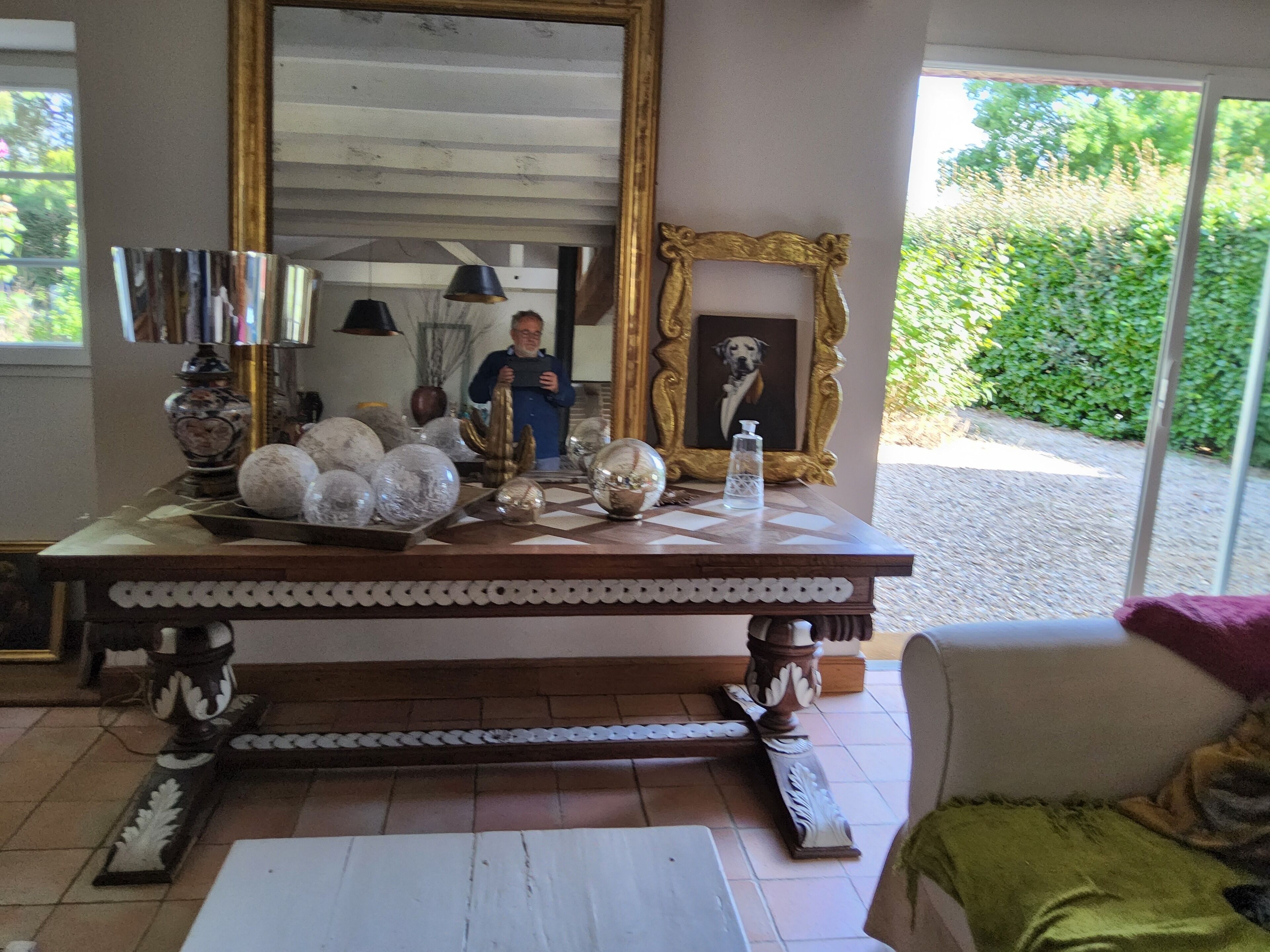 A room with a large mirror, a decorative table with various items, and a framed picture of a dog.