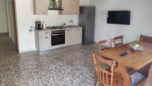 Une cuisine compacte équipée d’une cuisinière à gaz, d’un four et d’un réfrigérateur, ainsi que d’une table à manger avec des chaises et d’un téléviseur fixé au mur.